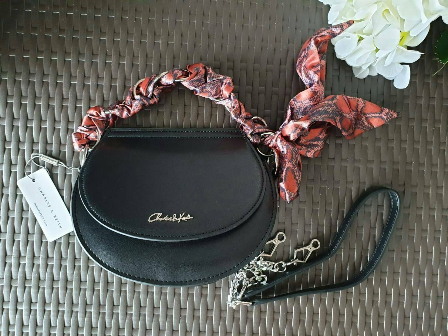 CHARLES & KEITH รุ่น LEATHER SATIN SCARF CROSSBODY BAG SL2-50150828 ราคาปกติช้อป ( ฿3,590.00 ) กระเป๋าถือ และ สะพาย ทรงโค้งมน หนังเรียบ ตั้งอยู่ทรง ด้านหน้าติดโลโก้แบรนด์ อะไหล่เงิน หูจับสายกระเป๋าร้อยเข้ากับห่วงเหล็กกลมๆ ด้วยผ้าลายสวยงามผูกเป็นโบว์เก๋ๆ ถ