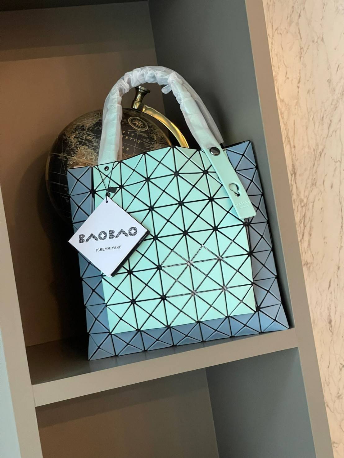 Baobao Issey Miyake Prism Kangaroo tote bag กระเป๋าถือทรงโท้ทที่ประดิษฐ์ขึ้นอย่างเชี่ยวชาญในญี่ปุ่น มาพร้อมแผงเรขาคณิตสำหรับการออกแบบที่ได้รับแรงบันดาลใจจากกระดาษพับ ซิลลูเอทอันเป็นเอกลักษณ์นี้ปิดท้ายด้วยสายรัดแบบอสมมาตร มีการพัฒนาโครงสร้างทรงสามเหลี่ยมเพ