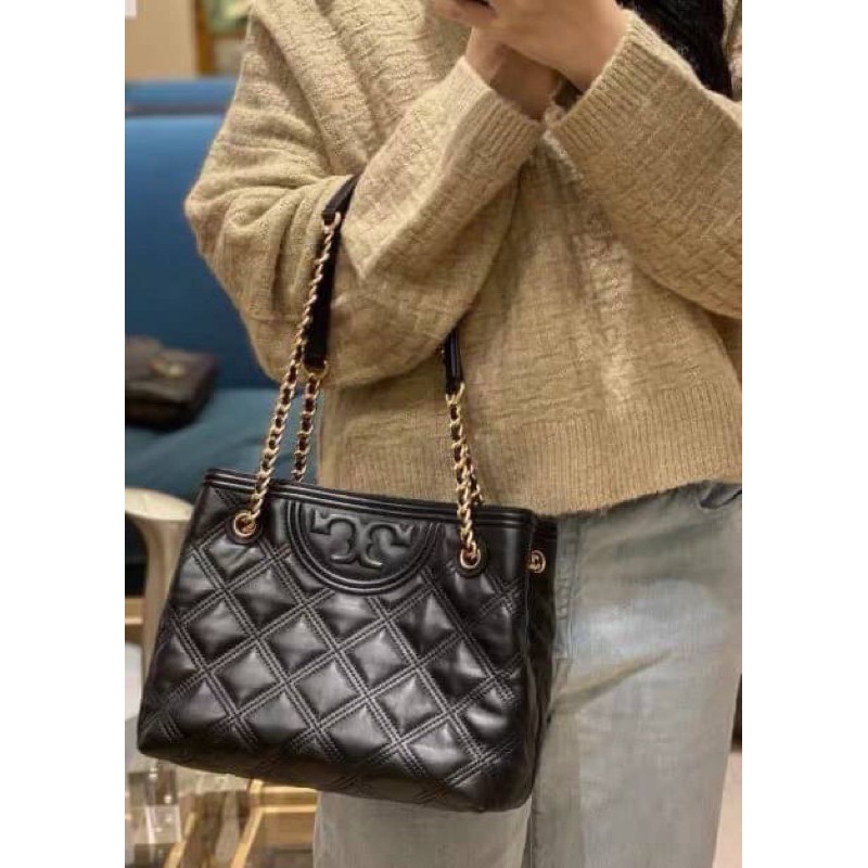 Tory Burch Fleming Soft Small Tote Bag เป็นกระเป๋าสะพายไหล่น่ารัก ๆ สักใบที่มีดีไซน์โดดเด่น สะดุดตา ใน Collection เรียกได้ว่าขายดีอันดับต้น ๆ ของแบรนด์ ใช้ได้ในลุคช์ทางการและกึ่งทางการ ดีเทลการตัดเย็บพิมพ์ลายนูนคู่กับแพทเทิร์นสี่เหลี่ยมทรงเพชร ที่ช่วยเพิ่