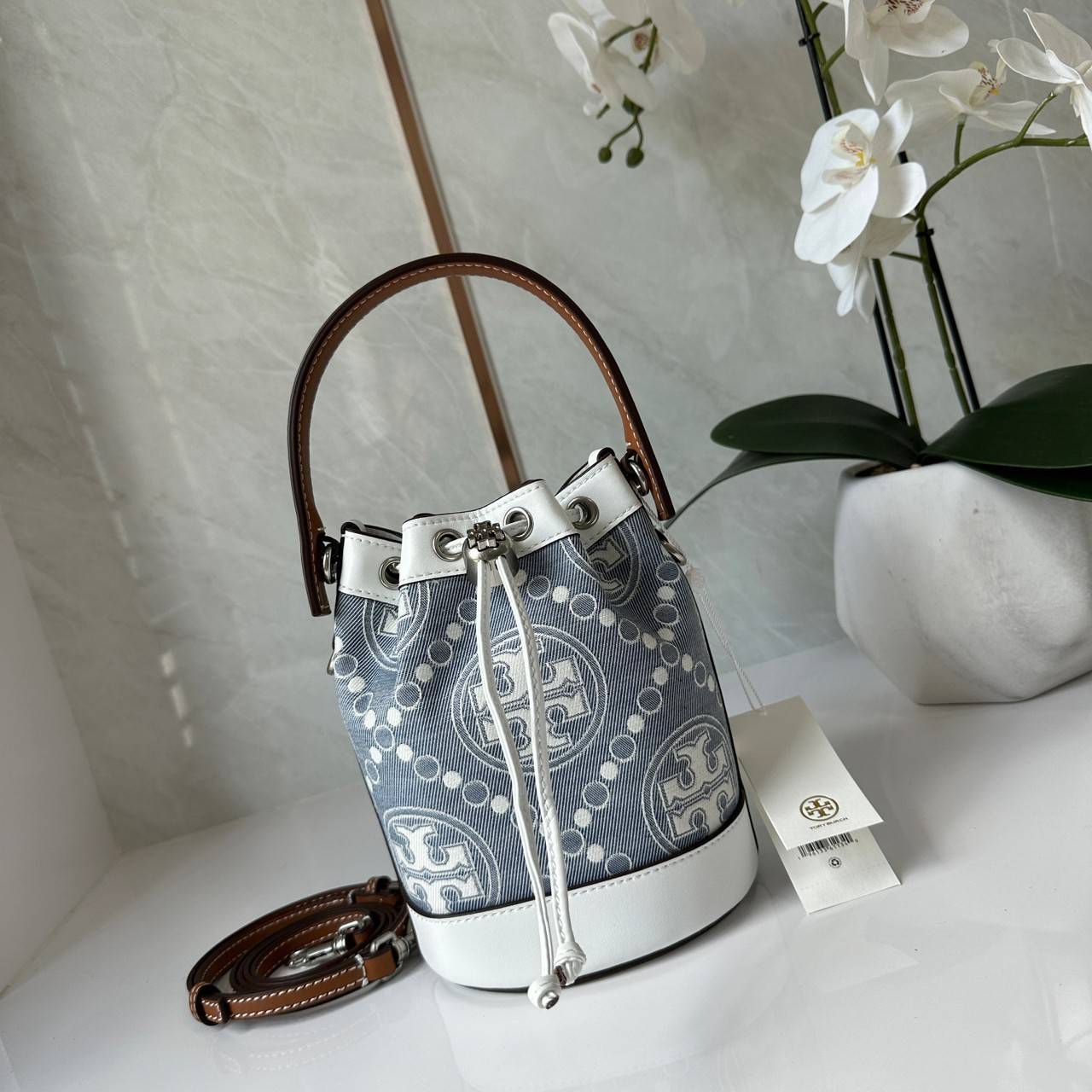 TORY BURCH Mini T Monogram Denim Bucket Bag คอลเลคชั่นใหม่ รูปแบบคลาสสิค พกพาความหรูหราไปได้ทุกที่ด้วยกระเป๋าทรง Bucket ขนาดกลางและปิดด้วยเชือกรูดพร้อมโลโก้แวววาว วัสดุผ้าเดนิมแจ็คการ์ด ตัดขอบหนังแท้ สวยหรู ทันสมัยสุดๆคะ