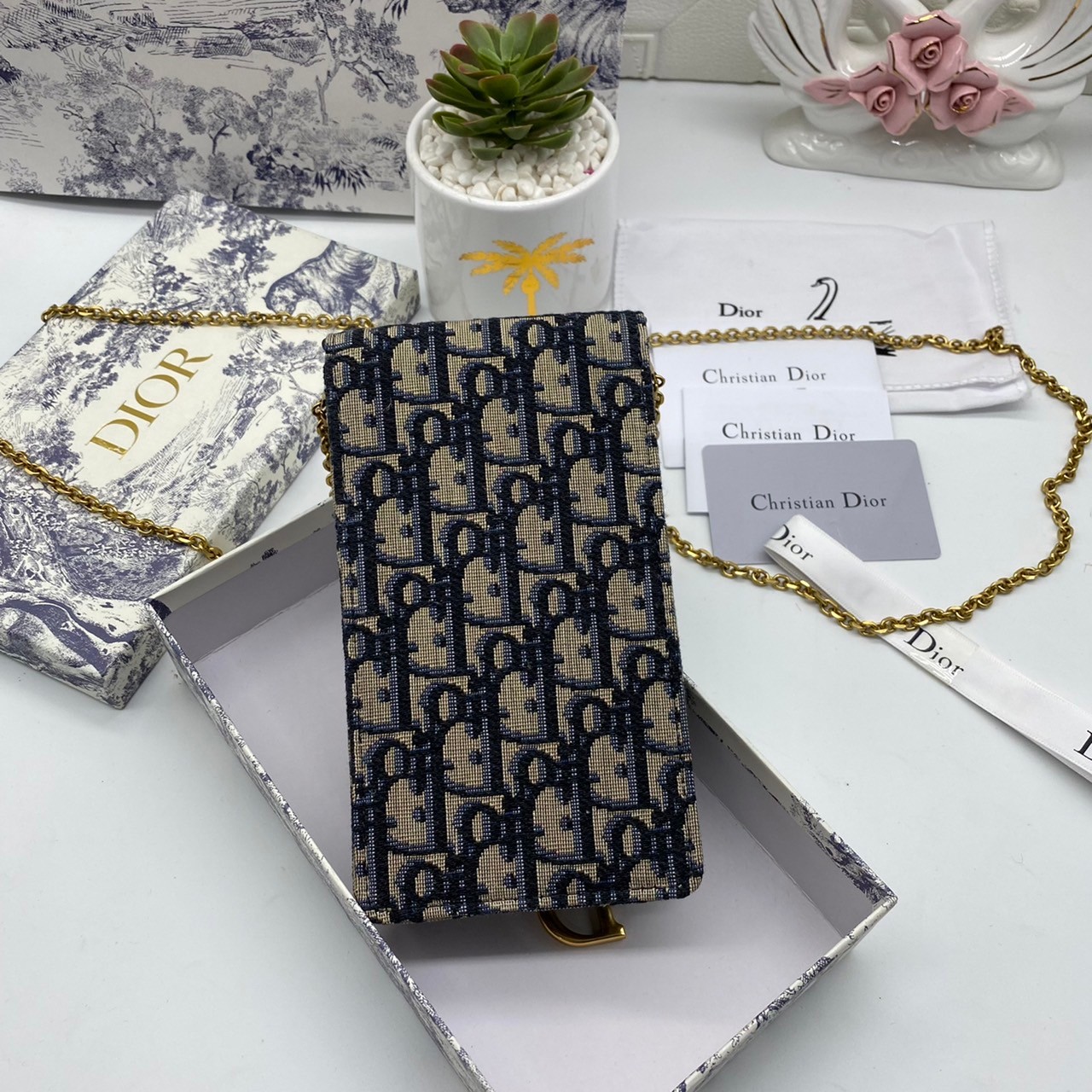 หนังแท้ DIOR PHONE BAG / DIOR PHONE HOLDER BAG กระเป๋าใส่โทรศัพท์เอกลักษณ์ของความหรู สายสะพายโซ่อะไหล่ทอง วัสดุหนังแท้และผ้า Jacquard อย่างดีสวยงามที่สุด ผสมผสานความสง่างามและคลาสสิกที่เข้ากับยุคสมัย ด้านหน้าโดดเด่นด้วยซิกเนเจอร์แบรนด์ เป็นอีกหนึ่งรุ่นที่