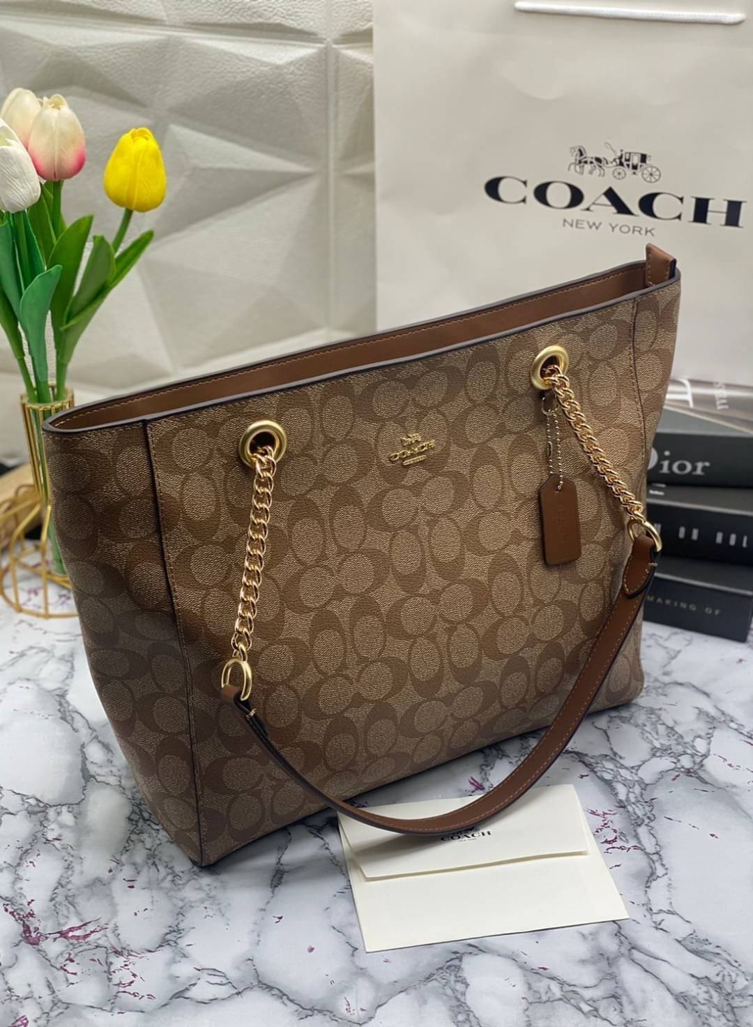 COACH Tote in Signature Canvas Bag กระเป๋าสะพายทรงช้อปปิ้ง สายกระเป๋าเป็นหนังสลับโซ่ทองสวยงาม เพิ่มความหรูหรา ภายในโล่งกว้างใส่ของได้เยอะมาก วัสดุ Canvas เคลือบลายซิกเนเจอร์และหนัง พร้อมซิปกลางเก็บของได้มิดชิดเลยค่ะ มี 3 สี น้ำตาล ดำ ขาว