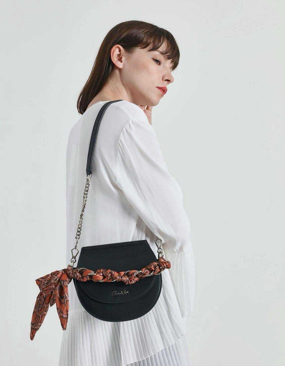 CHARLES & KEITH รุ่น LEATHER SATIN SCARF CROSSBODY BAG SL2-50150828 ราคาปกติช้อป ( ฿3,590.00 ) กระเป๋าถือ และ สะพาย ทรงโค้งมน หนังเรียบ ตั้งอยู่ทรง ด้านหน้าติดโลโก้แบรนด์ อะไหล่เงิน หูจับสายกระเป๋าร้อยเข้ากับห่วงเหล็กกลมๆ ด้วยผ้าลายสวยงามผูกเป็นโบว์เก๋ๆ ถ