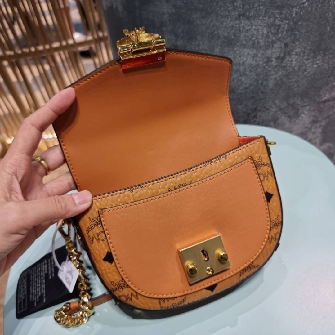 M.C.M MINI PATRICIA CROSSBODY IN VISETOS กระเป๋าสะพายไซส์มินิ แรงดีไม่มีตกน้า คอลเลคชั่นนี้ดีไซน์แปลกใหม่ ทรงโค้งมน สวยหรู ด้านข้างตกแต่งหมุดทองรอบใบ วัสดุตัวกระเป๋าเป็นหนังแคนวาสคุณภาพดี ภายในเป็นหนังกลับสีส้มโดดเด่นเป็นเอกลักษณ์ มีช่องใส่บัตรแยกให้ เปิด