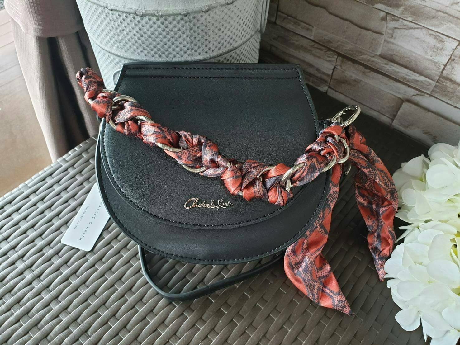 CHARLES & KEITH รุ่น LEATHER SATIN SCARF CROSSBODY BAG SL2-50150828 ราคาปกติช้อป ( ฿3,590.00 ) กระเป๋าถือ และ สะพาย ทรงโค้งมน หนังเรียบ ตั้งอยู่ทรง ด้านหน้าติดโลโก้แบรนด์ อะไหล่เงิน หูจับสายกระเป๋าร้อยเข้ากับห่วงเหล็กกลมๆ ด้วยผ้าลายสวยงามผูกเป็นโบว์เก๋ๆ ถ