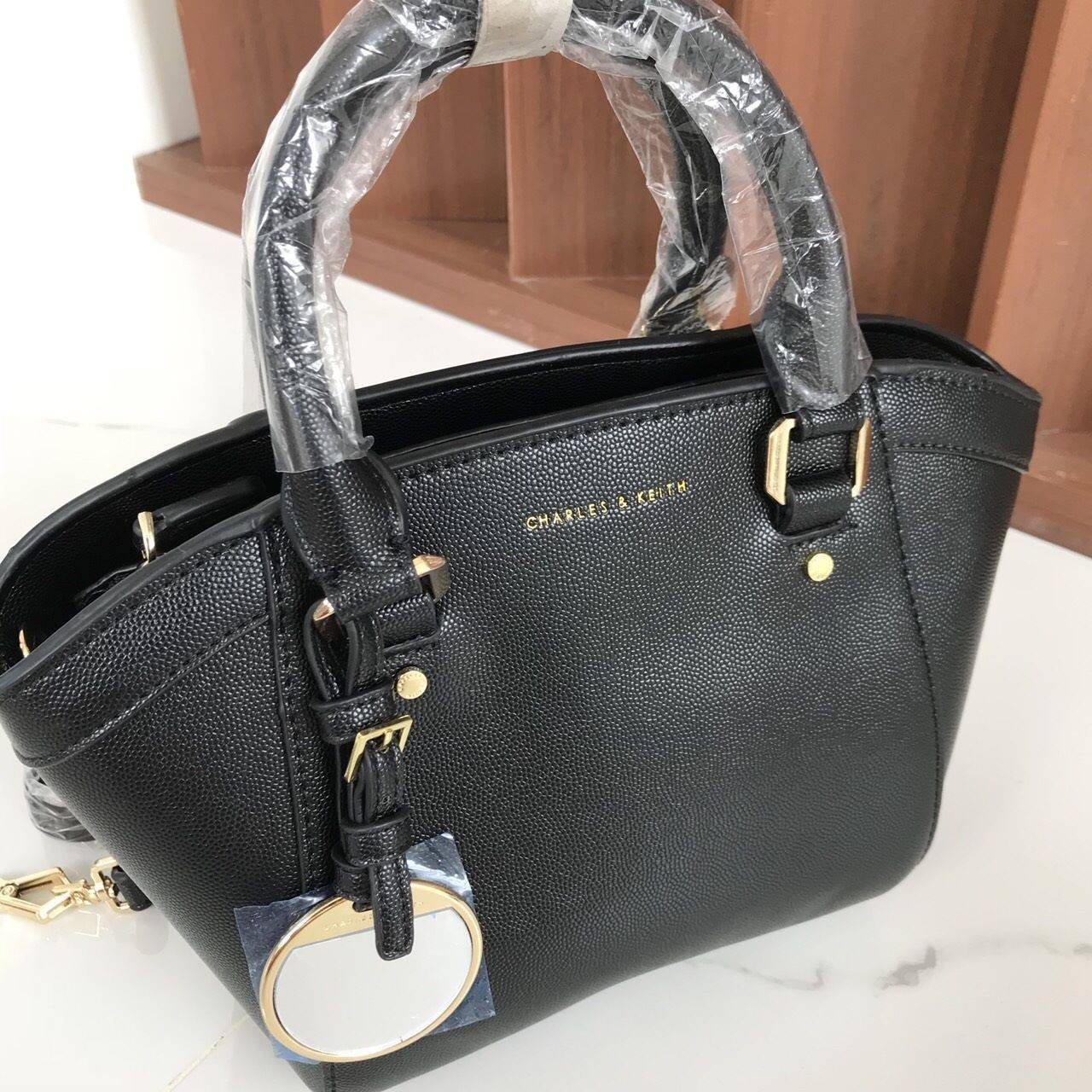 CHARLES & KEITH CITY BAG กระเป๋าถือหรือสะพาย ตั้งอยู่ทรงสวย มีโลหะรองฐาน เปิดปิดด้วยซิปเดียว ภายในมี 2 ช่องเล็กด้านหน้าประดับด้วยกระจกทรงกลม ใช้งานได้จริง ปั้มโลโก้แบรนด์ มาพร้อมสายสะพายยาว ปรับระดับและถอดสายได้ หูพับลงได้ น้ำหนักเบา ต้องมีไว้ครอบครองสักใ
