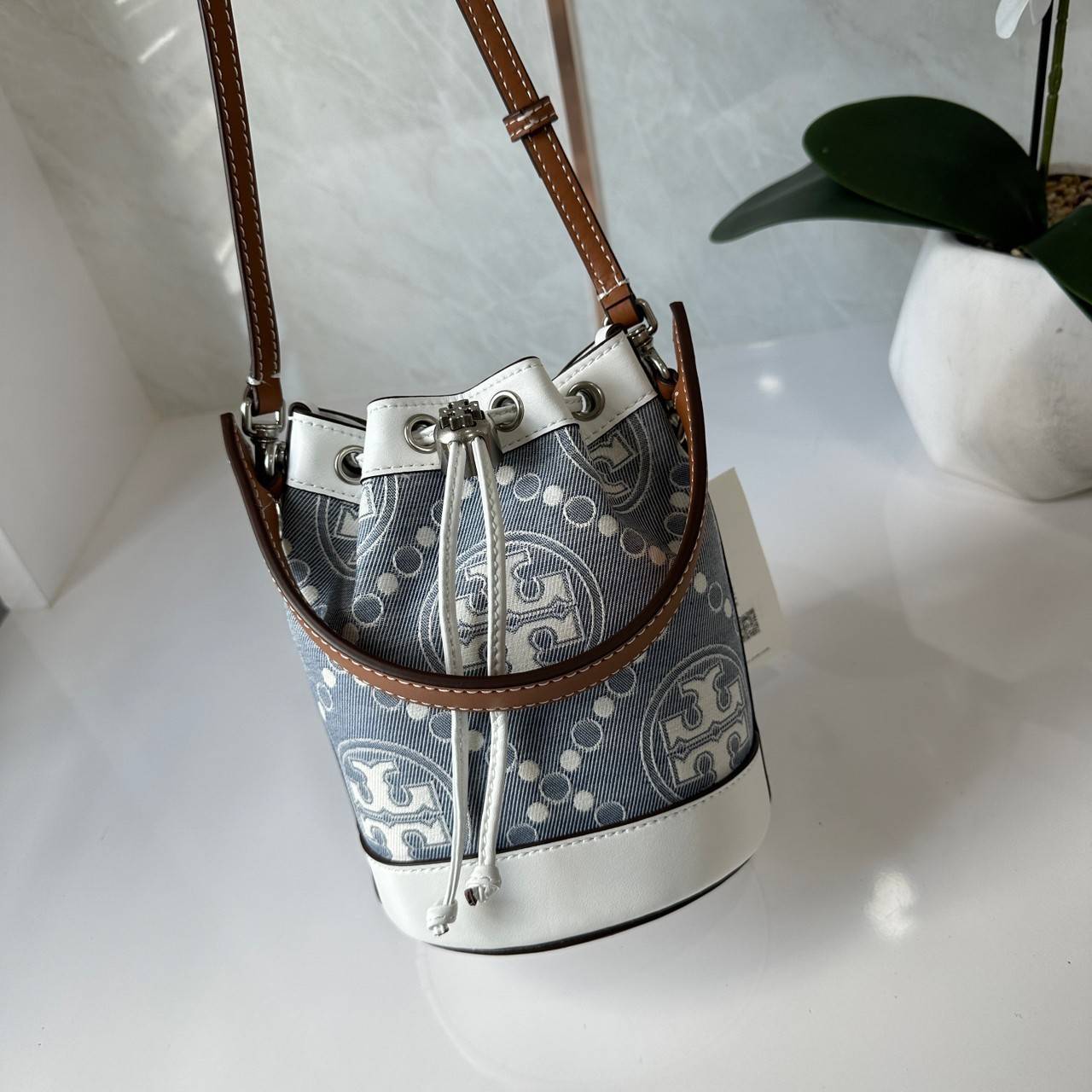 TORY BURCH Mini T Monogram Denim Bucket Bag คอลเลคชั่นใหม่ รูปแบบคลาสสิค พกพาความหรูหราไปได้ทุกที่ด้วยกระเป๋าทรง Bucket ขนาดกลางและปิดด้วยเชือกรูดพร้อมโลโก้แวววาว วัสดุผ้าเดนิมแจ็คการ์ด ตัดขอบหนังแท้ สวยหรู ทันสมัยสุดๆคะ