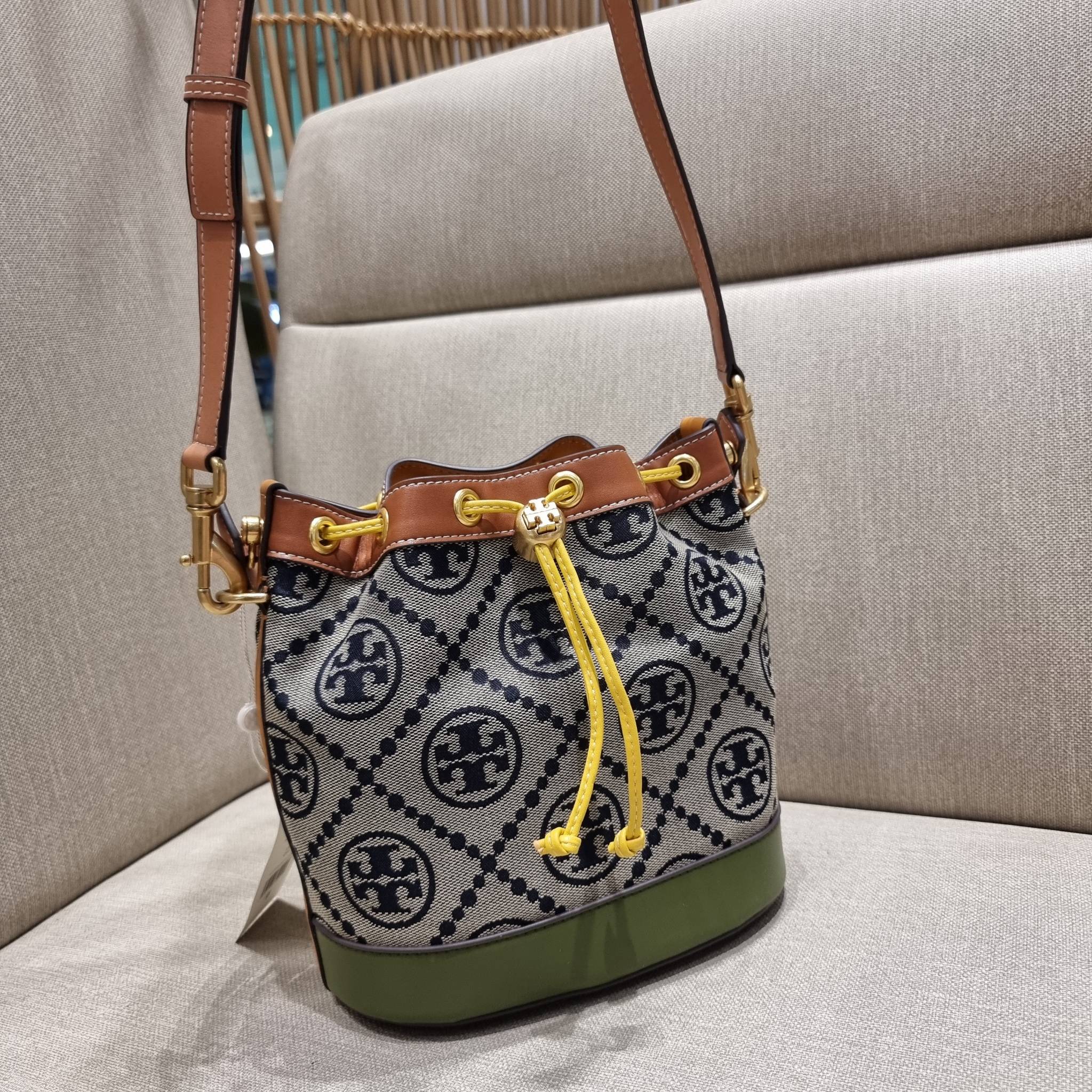 TORY BURCH T MONOGRAM COLORBLOCK JACQUARD BUCKET BAG ไอเท็มใหม่ที่ใครๆก็รอ กระเป๋าบัคเก็ตทรงสวย ที่ยังคงให้ความโดดเด่นด้วยลวดลายเอกลักษณ์ เพิ่มเติมดีไซน์บล็อคสี ตัดกันได้อย่างลงตัว ถักทอบนวัสดุ woven jacquard ลายคมชัด สลับส่วนของหนังแท้ ภายในเป็นช่องโล่งก