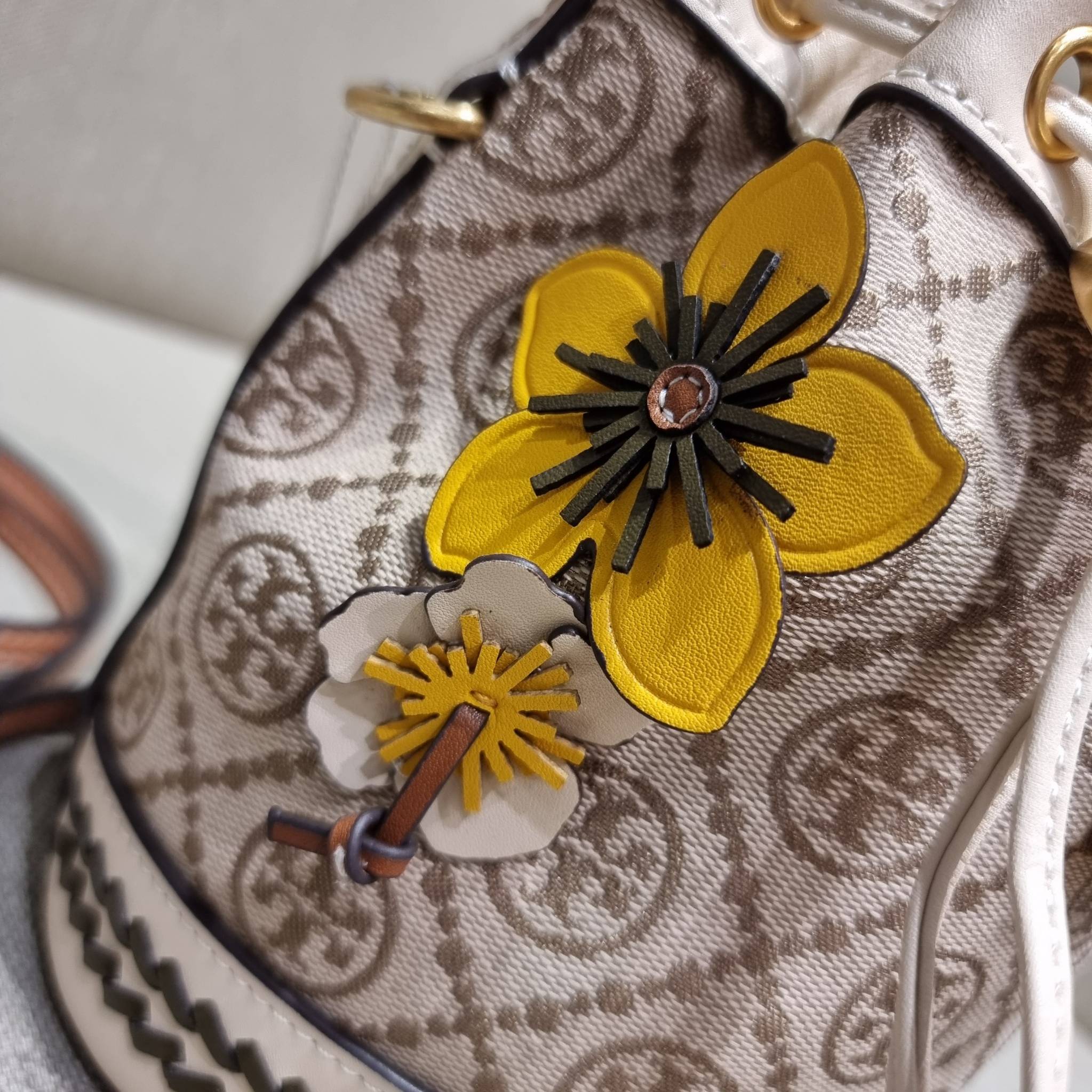 TORY BURCH MINI T MONOGRAM FLORAL BUCKET BAG คอลเลคชั่นใหม่ พร้อมเสิร์ฟความสวยให้ถึงบ้าน!! กระเป๋าบัคเก็ตทรงยอดนิยม ไซส์มินิ ดีไซน์ใหม่ล่าสุด สไตล์งานคราฟ มีลูกเล่นประดับดอกไม้กับตัวกระเป๋า และตัวรูดสาย วัสดุผ้า jacquard ตัดสลับหนังแท้ หูจับและขอบกระเป๋าต