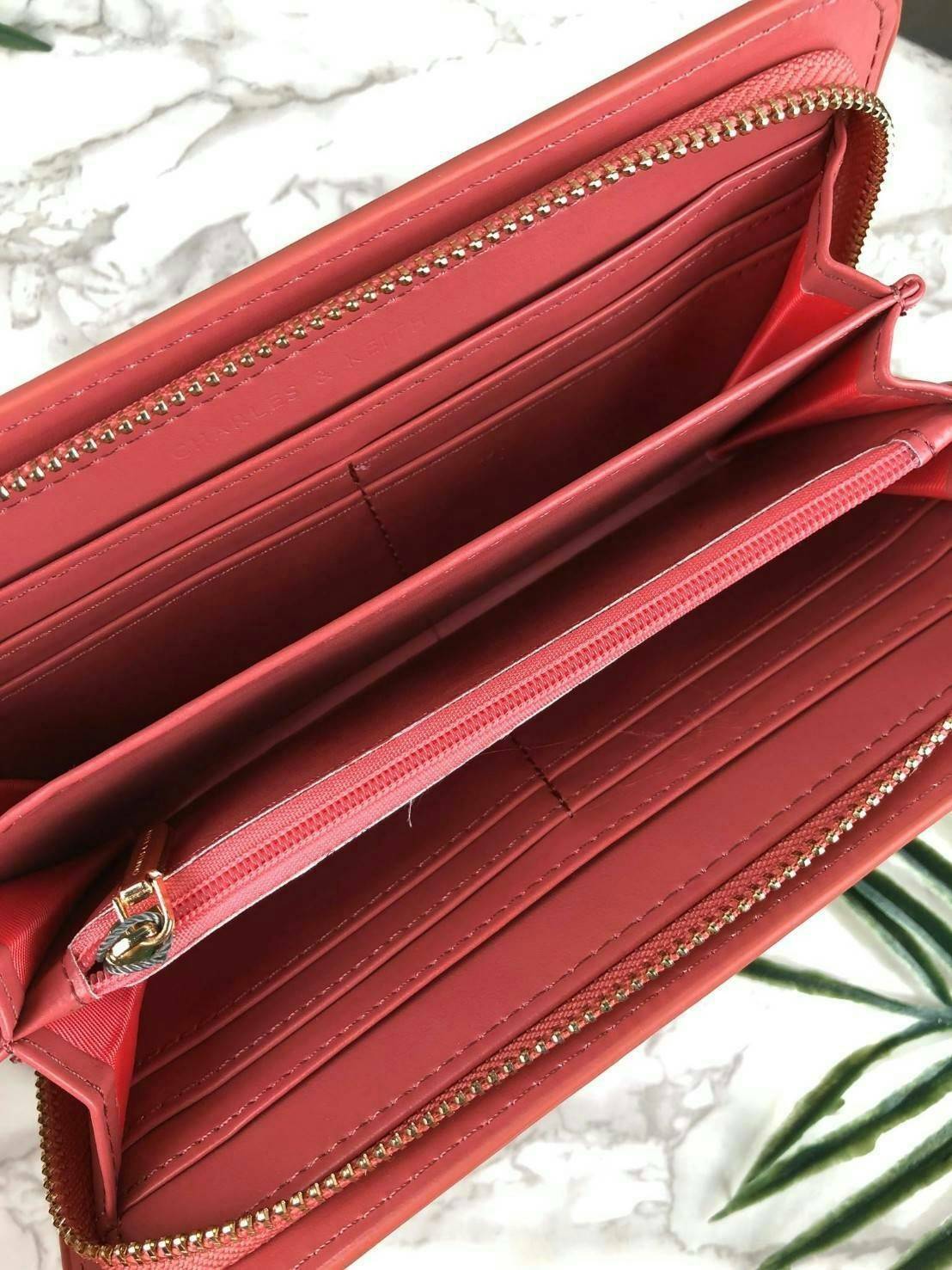 CHARLES & KEITH CLASSIC ZIP AROUND WALLET กระเป๋าเงินใบยาวซิปรอบ มีสายคล้องมีสีเข้ากระเป๋า 1 เส้น ใช้งานง่ายมากๆ คล้องมือก็เก๋ ด้านหน้าปั๊มโลโก้แบรนด์ เปิดปิดด้วยซิปรอบ ที่สายคล้องมือแต่งหมุดสีสวยเด่น ถอดสายได้ จุบัตรได้ 12 ใบ มีช่องซิปใส่เหรียญและช่องใส่