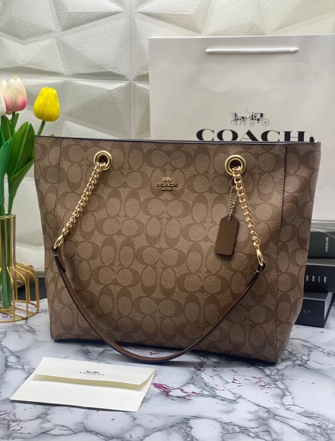 COACH Tote in Signature Canvas Bag กระเป๋าสะพายทรงช้อปปิ้ง สายกระเป๋าเป็นหนังสลับโซ่ทองสวยงาม เพิ่มความหรูหรา ภายในโล่งกว้างใส่ของได้เยอะมาก วัสดุ Canvas เคลือบลายซิกเนเจอร์และหนัง พร้อมซิปกลางเก็บของได้มิดชิดเลยค่ะ มี 3 สี น้ำตาล ดำ ขาว