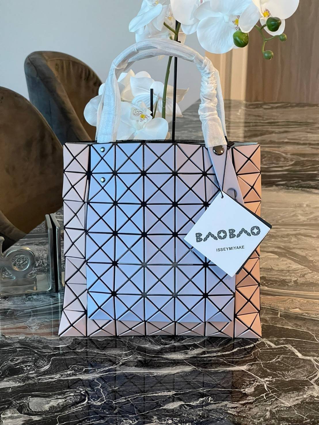 Baobao Issey Miyake Prism Kangaroo tote bag กระเป๋าถือทรงโท้ทที่ประดิษฐ์ขึ้นอย่างเชี่ยวชาญในญี่ปุ่น มาพร้อมแผงเรขาคณิตสำหรับการออกแบบที่ได้รับแรงบันดาลใจจากกระดาษพับ ซิลลูเอทอันเป็นเอกลักษณ์นี้ปิดท้ายด้วยสายรัดแบบอสมมาตร มีการพัฒนาโครงสร้างทรงสามเหลี่ยมเพ