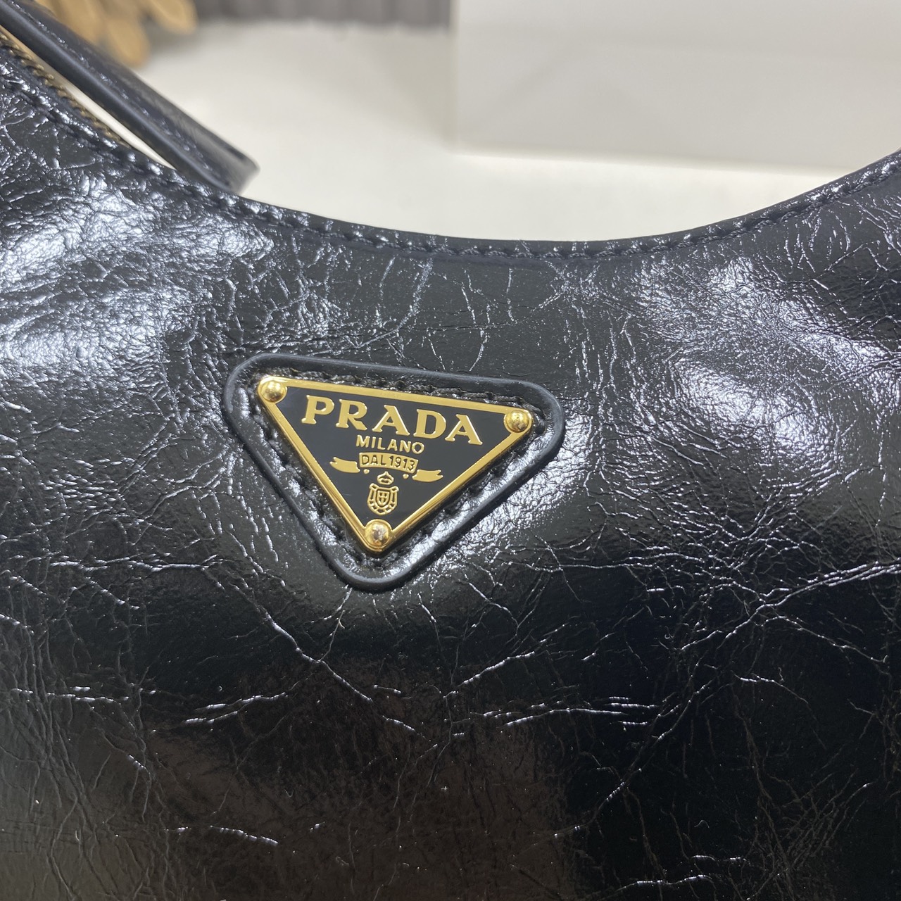 ORI หนังแท้ | Prada Re-Edition 2005 bag in Naplak leather กระเป๋าสะพายทรงโฮโบหนังแก้ว ดีไซน์เอฟเฟกต์มันวาวและเท็กซ์เจอร์ที่มีเสน่ห์สไตล์วินเทจ พร้อมทริกห้อยเพิ่มสไตล์สัมผัสที่โดดเด่นและร่วมสมัยยิ่งขึ้น