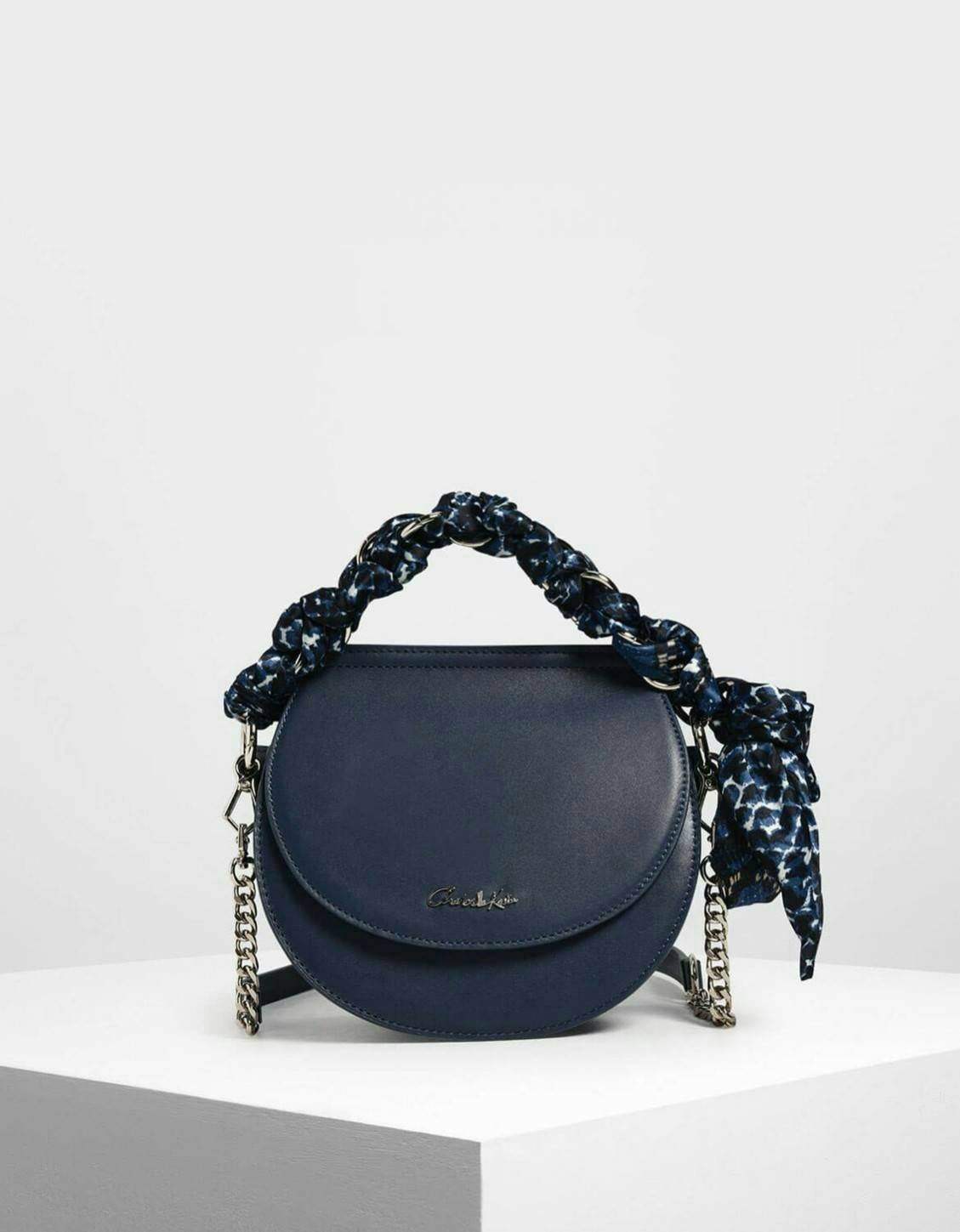 CHARLES & KEITH รุ่น LEATHER SATIN SCARF CROSSBODY BAG SL2-50150828 ราคาปกติช้อป ( ฿3,590.00 ) กระเป๋าถือ และ สะพาย ทรงโค้งมน หนังเรียบ ตั้งอยู่ทรง ด้านหน้าติดโลโก้แบรนด์ อะไหล่เงิน หูจับสายกระเป๋าร้อยเข้ากับห่วงเหล็กกลมๆ ด้วยผ้าลายสวยงามผูกเป็นโบว์เก๋ๆ ถ