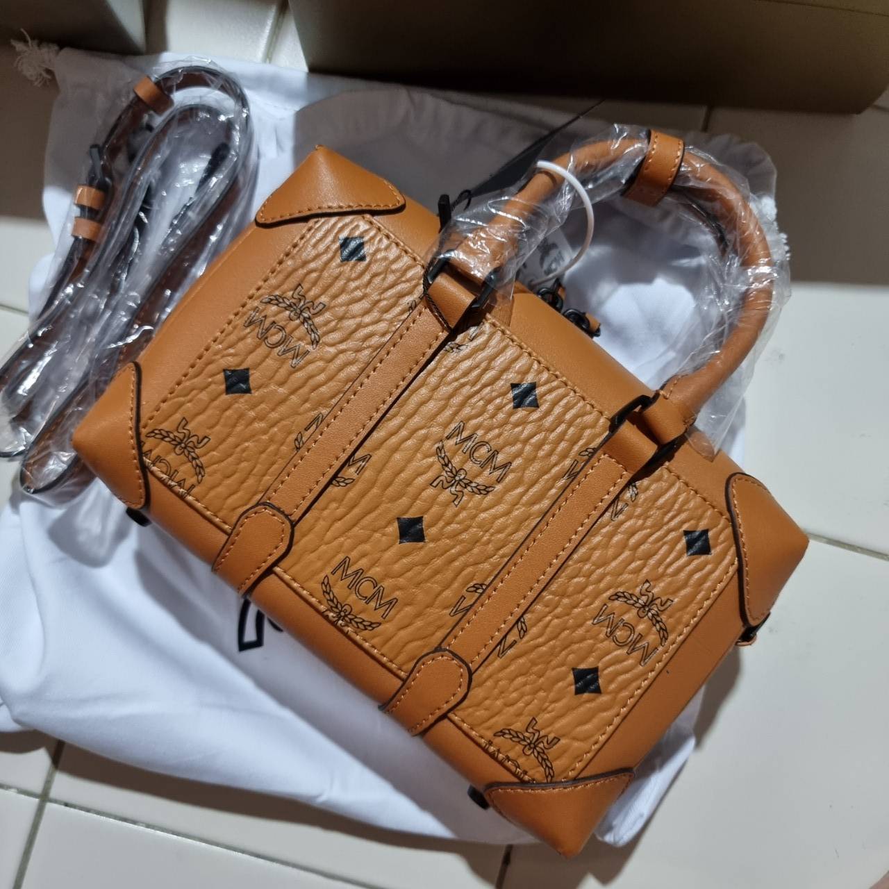 M.C.M SMALL E/W SOFT BERLIN CROSSBODY IN VISETOS ไอเท็มใหม่ในดีไซน์ทรงกระเป๋าเดินทางแบบคลาสสิค ย่อส่วนมาให้ใช้งานได้แบบสบายๆ พกพาสะดวก แมทช์ได้ทุกสไตล์ ใช้ได้แบบ unisex ใช้งานง่ายด้วยหูจับในตัว และซิปหลัก อะไหล่สีดำดูมีมิติตัดกับสีน้ำตาลคอนยัคได้เป็นอย่าง